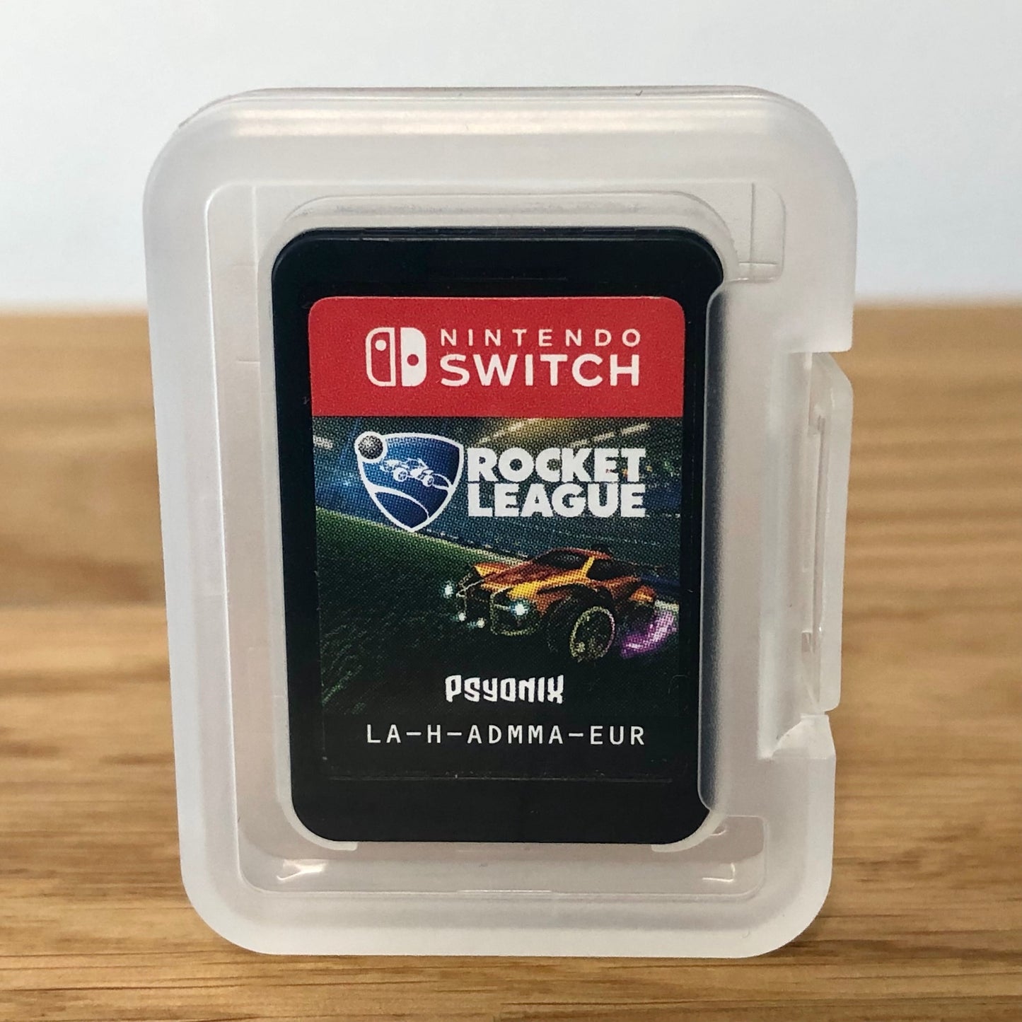 Cartridge of Rocket League for Nintendo Switch, the cartridge is inside a cartridge size transparent protective case, through which you can see the front of the cartridge