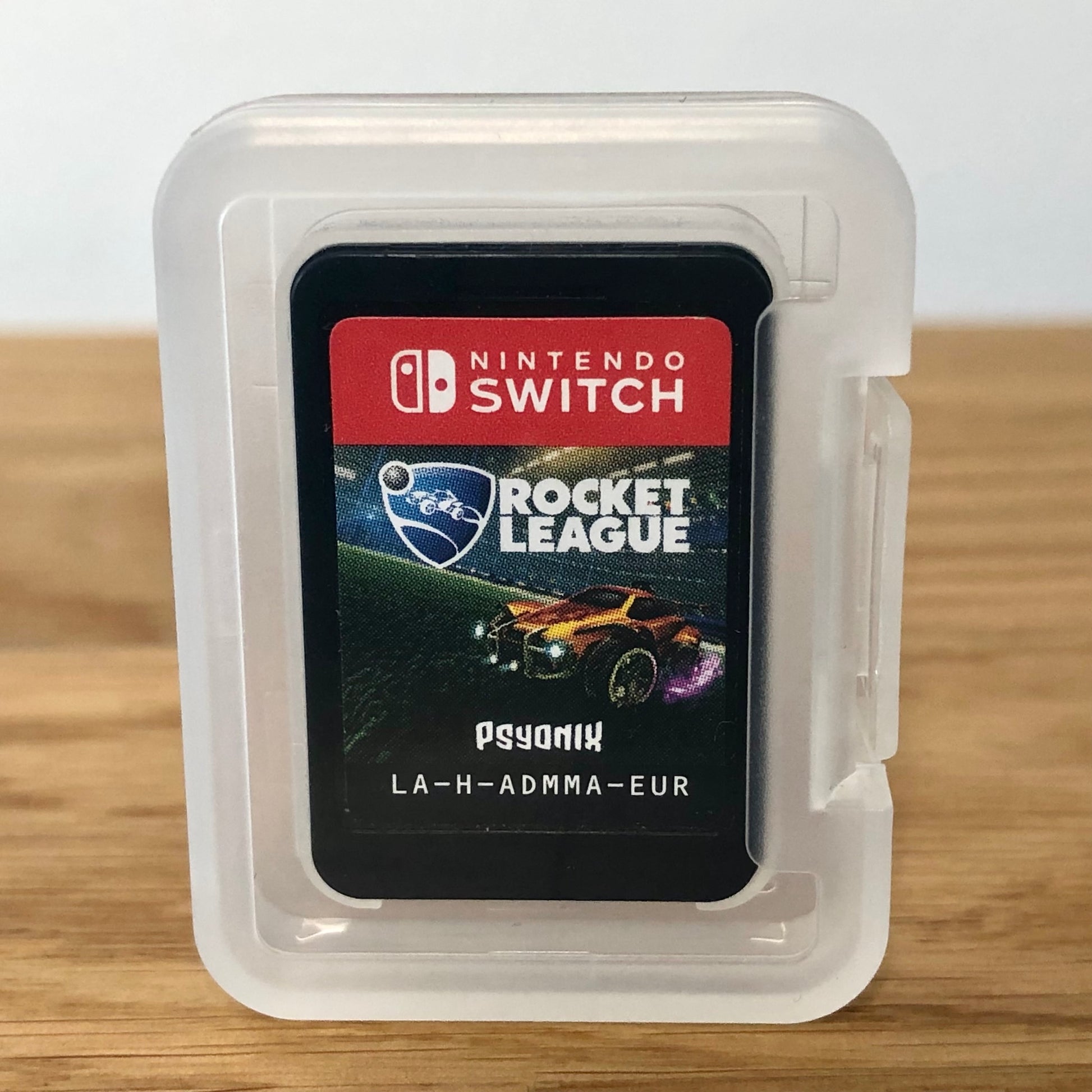 Cartridge of Rocket League for Nintendo Switch, the cartridge is inside a cartridge size transparent protective case, through which you can see the front of the cartridge