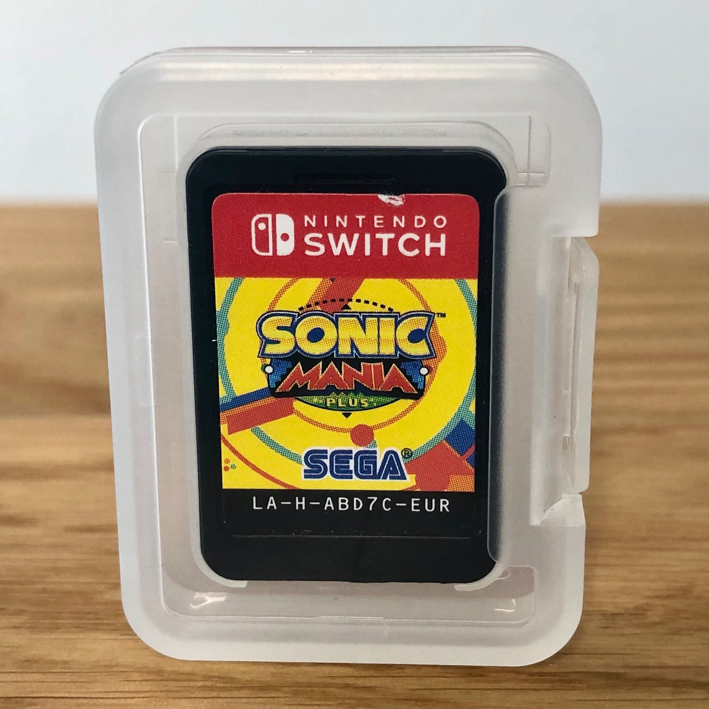 Cartridge of Sonic Mania Plus for Nintendo Switch, the cartridge is inside a cartridge size transparent protective case, through which you can see the front of the cartridge