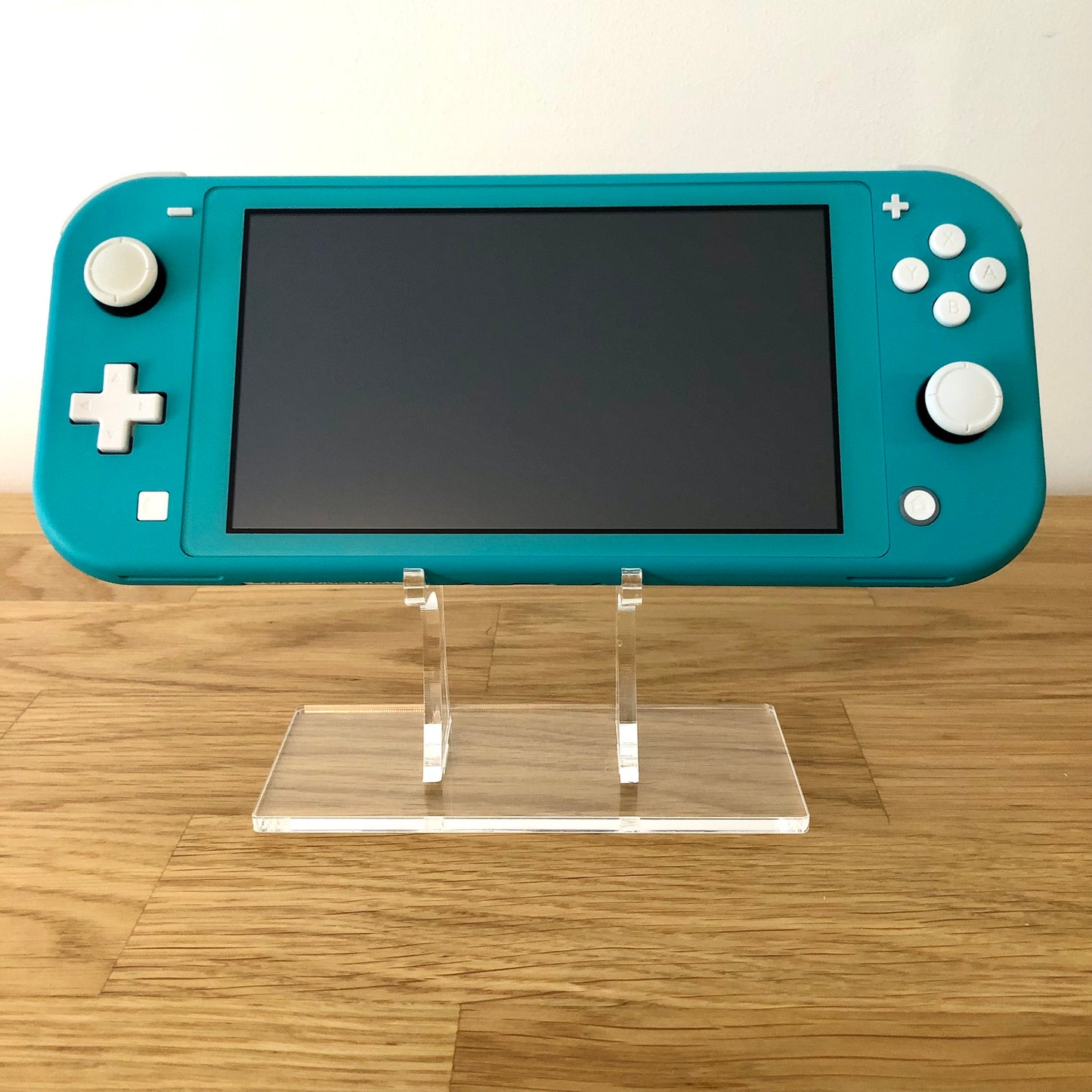 Front view of Turquoise Nintendo Switch Lite console turned off, positioned upright on a clear display stand.