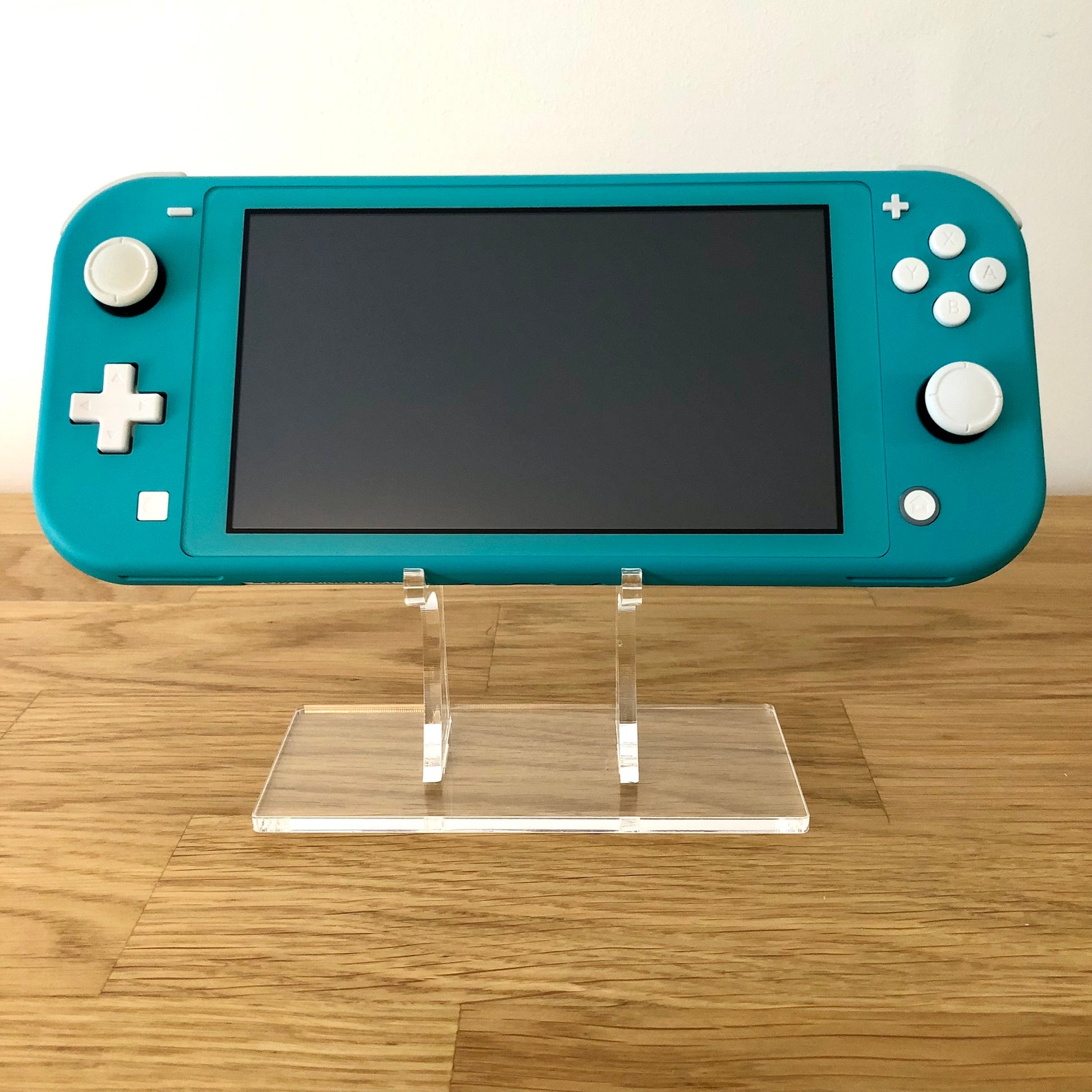 Front view of Turquoise Nintendo Switch Lite console turned off, positioned upright on a clear display stand.