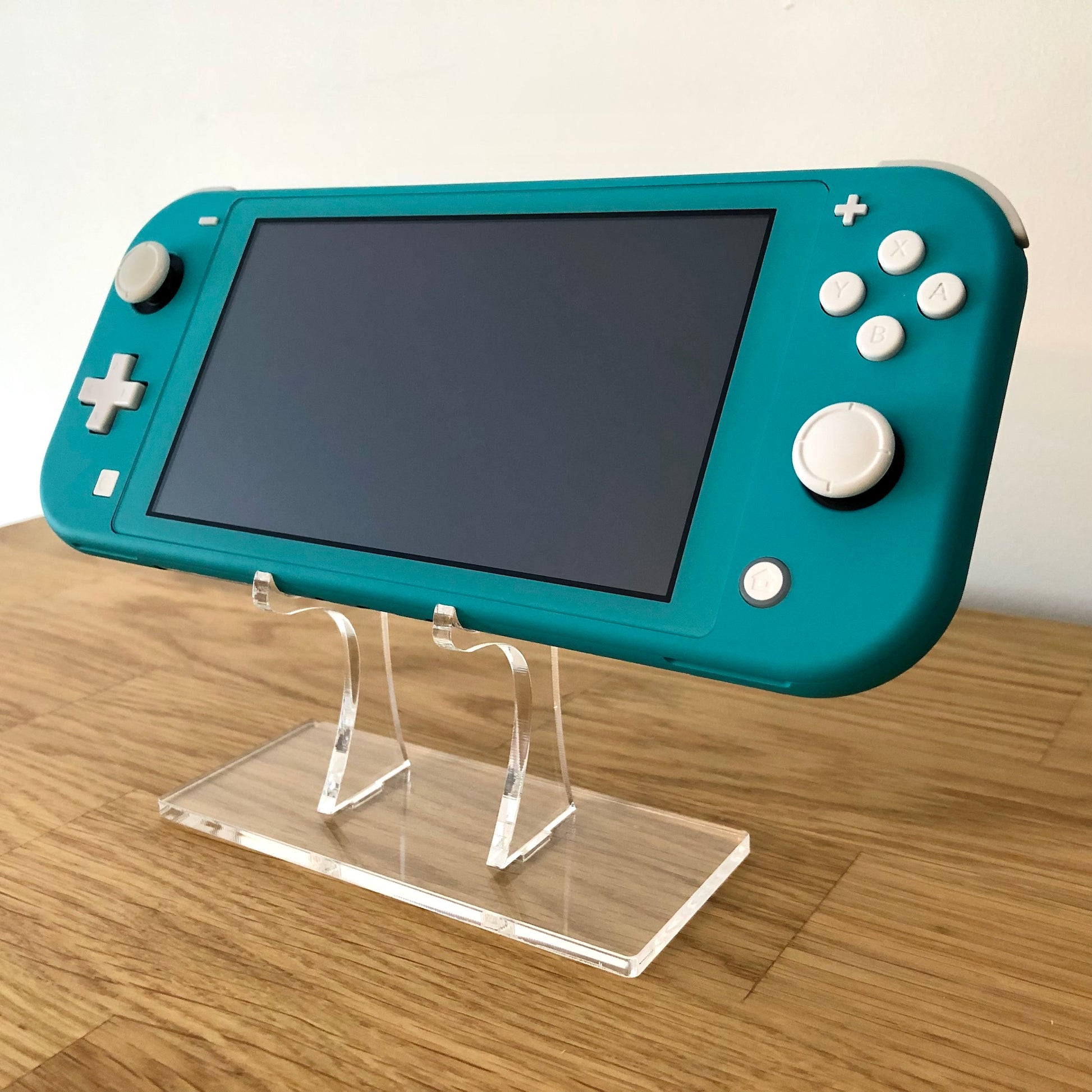 Angled front view of Turquoise Nintendo Switch Lite showing buttons, thumb sticks and screen on clear stand.