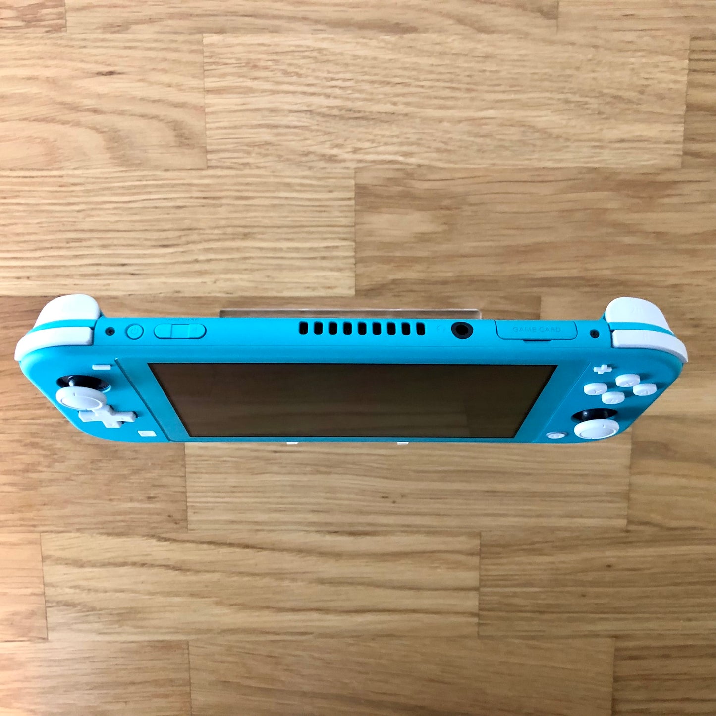 Top view of Turquoise Nintendo Switch Lite console showing volume, power, headphone jack and game card slot.