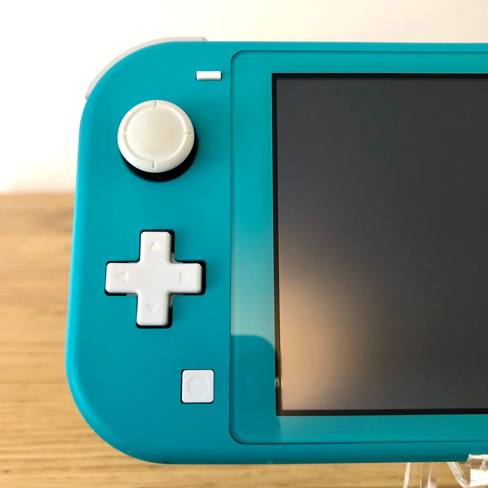 Close-up of left side of Turquoise Nintendo Switch Lite showing joystick, D-pad, and capture button.