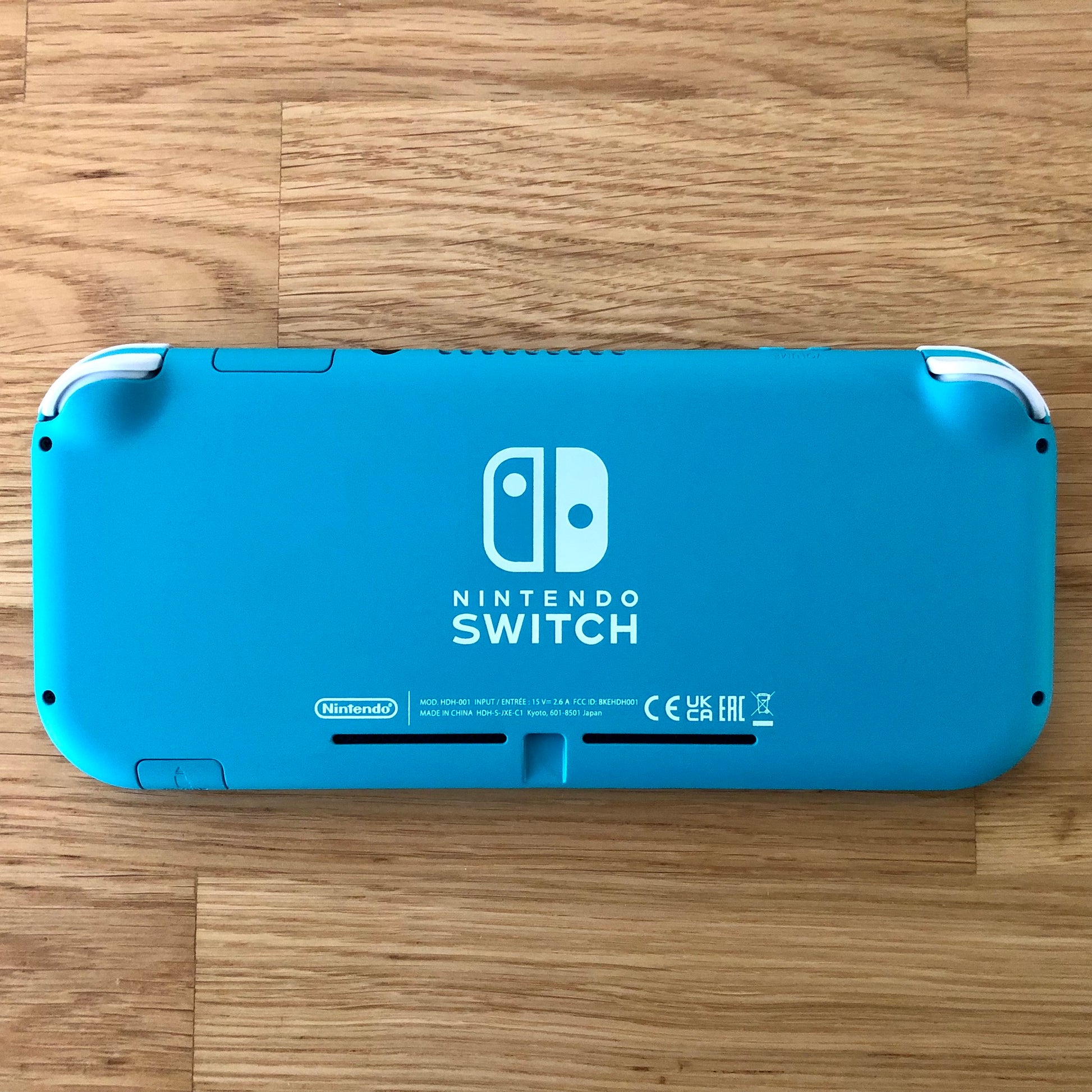 Back of Turquoise Nintendo Switch Lite console placed flat, with logos, text and condition clearly shown.