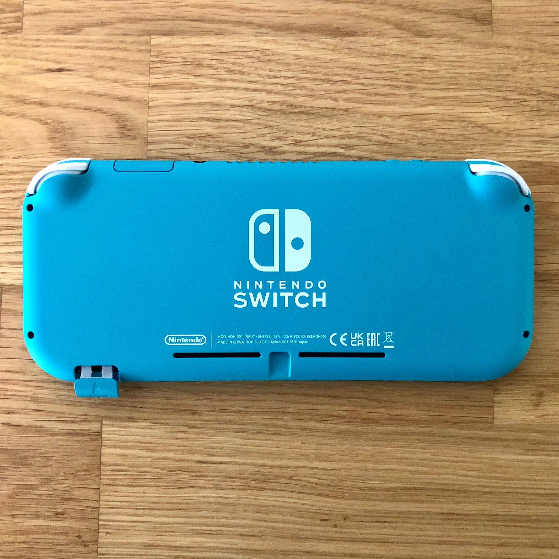 Turquoise Nintendo Switch Lite console laid flat with microSD slot cover open, showing full back design.