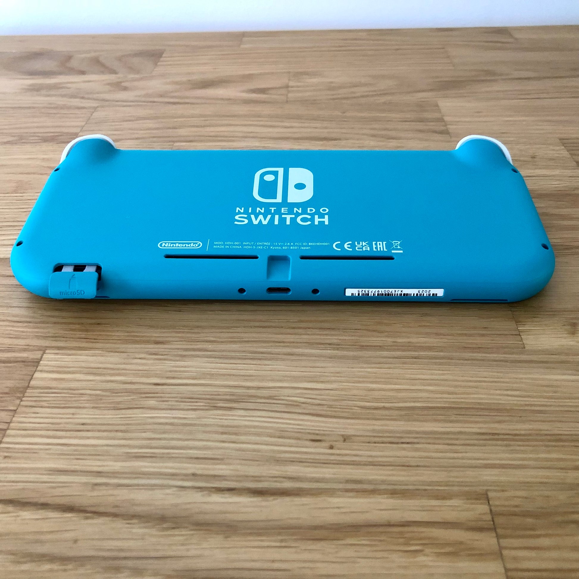 Angled bottom view of Turquoise Nintendo Switch Lite console showing charging port, serial number and microSD slot.