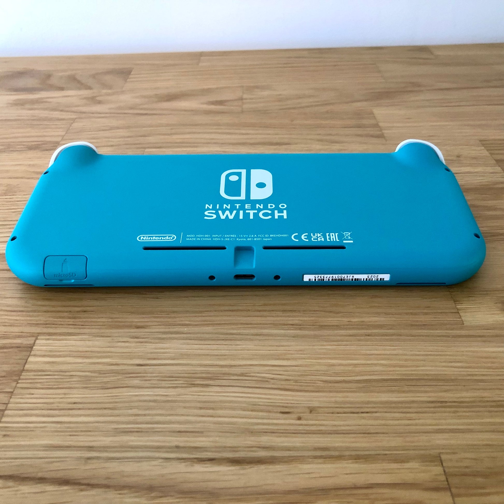 Back of Nintendo Switch Lite in Turquoise, showing microSD slot, USB-C port, and product markings on a wooden surface.