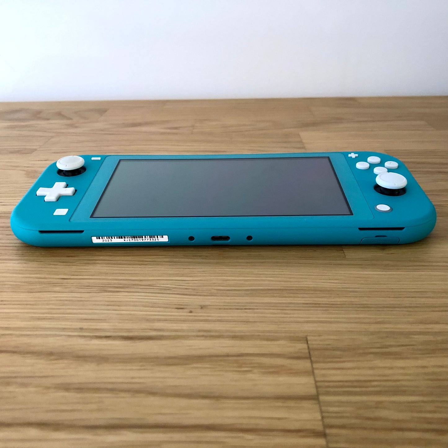 Bottom edge view of turquoise Nintendo Switch Lite showing USB-C charging port, speakers, game card slot cover, and all face buttons.
