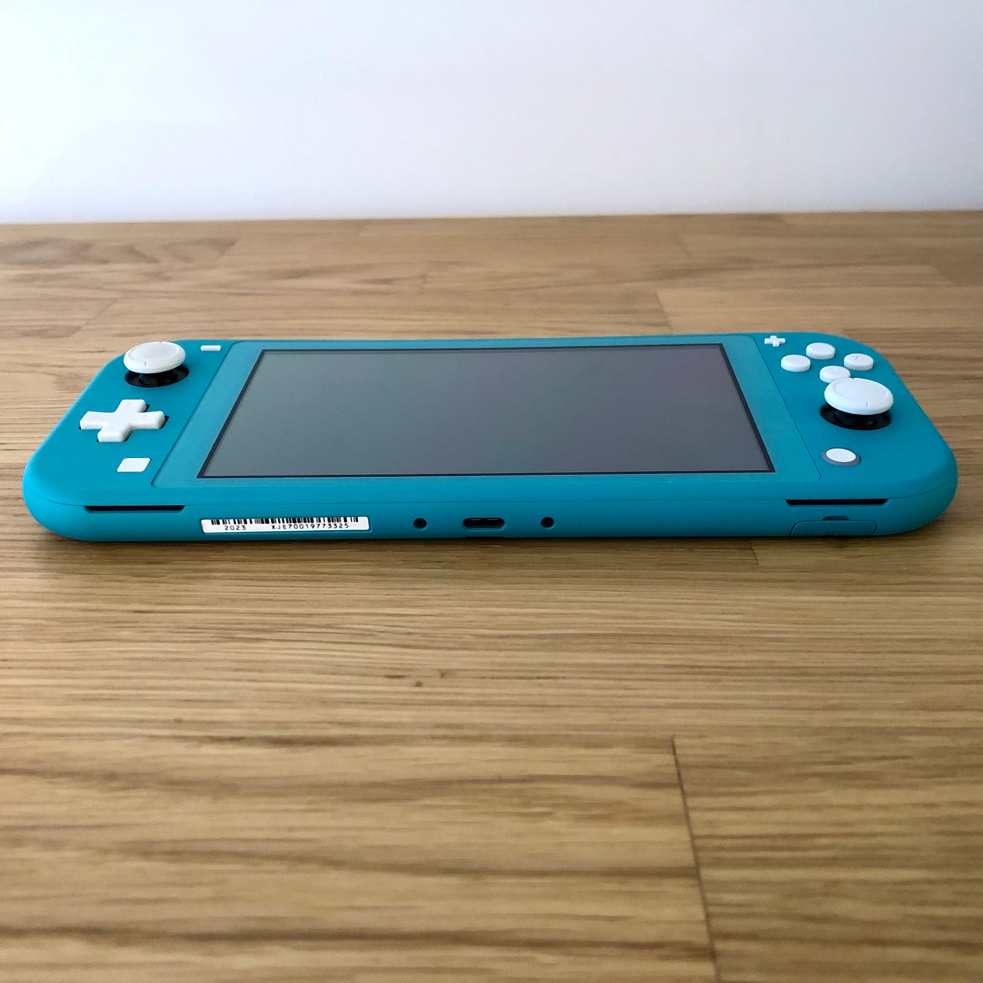 Bottom edge view of turquoise Nintendo Switch Lite showing USB-C charging port, speakers, game card slot cover, and all face buttons.