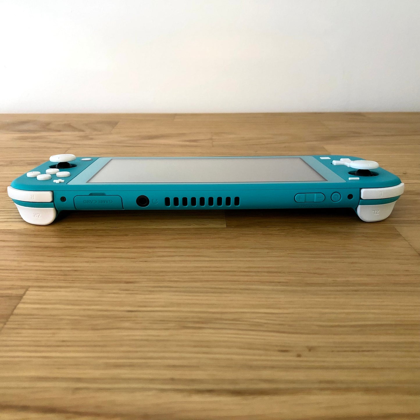 Top edge view of turquoise Nintendo Switch Lite with game card slot, headphone jack, vent, and shoulder buttons visible.