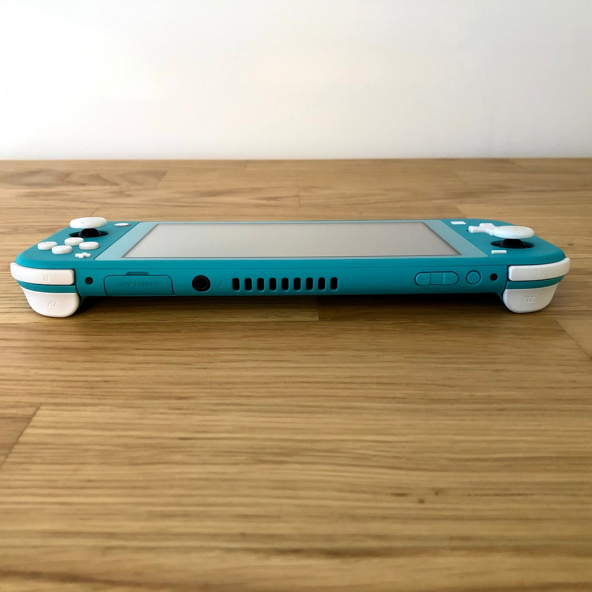 Top edge view of turquoise Nintendo Switch Lite with game card slot, headphone jack, vent, and shoulder buttons visible.