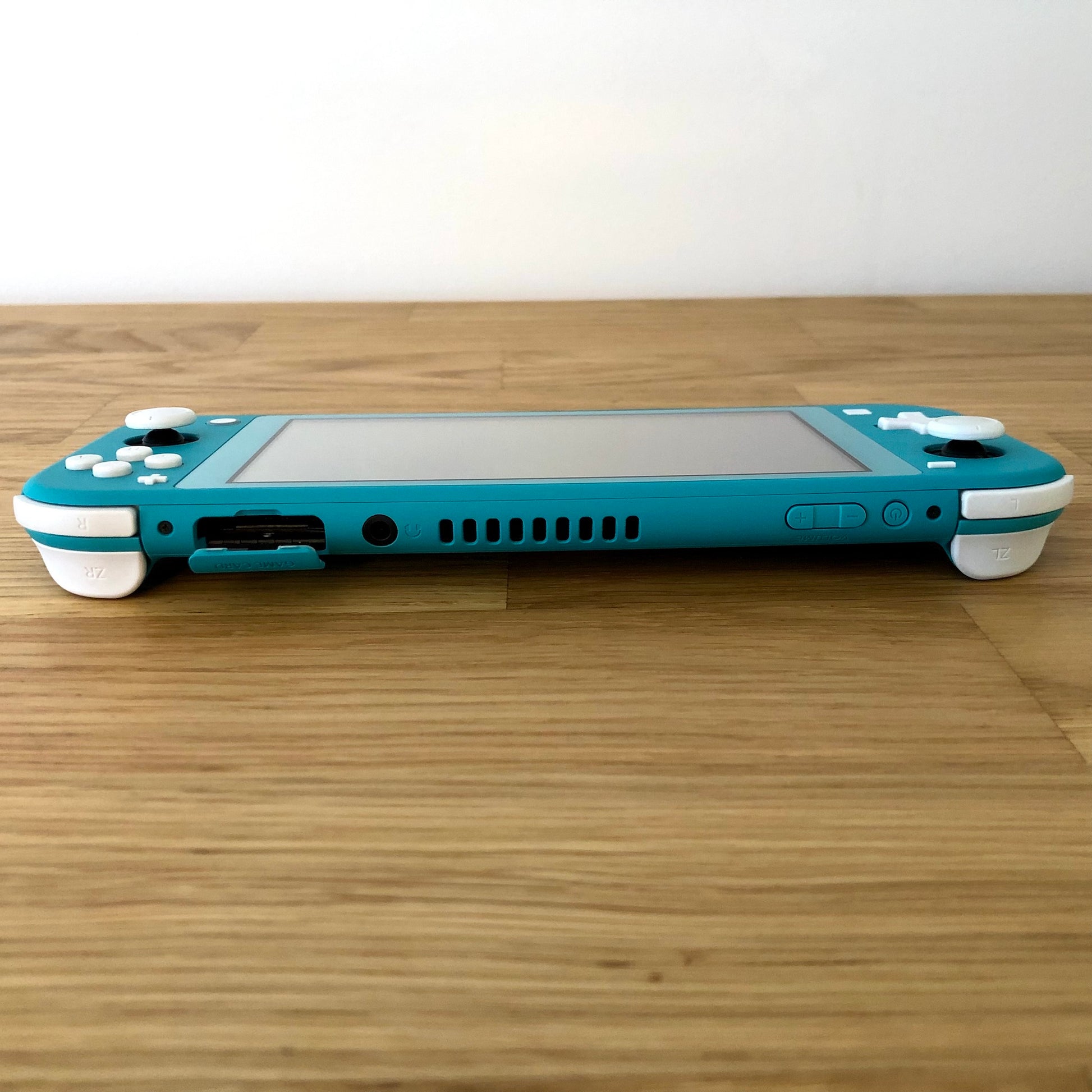 Flat top edge shot of turquoise Nintendo Switch Lite showing all buttons, ports, vent, and shoulder triggers in full view.