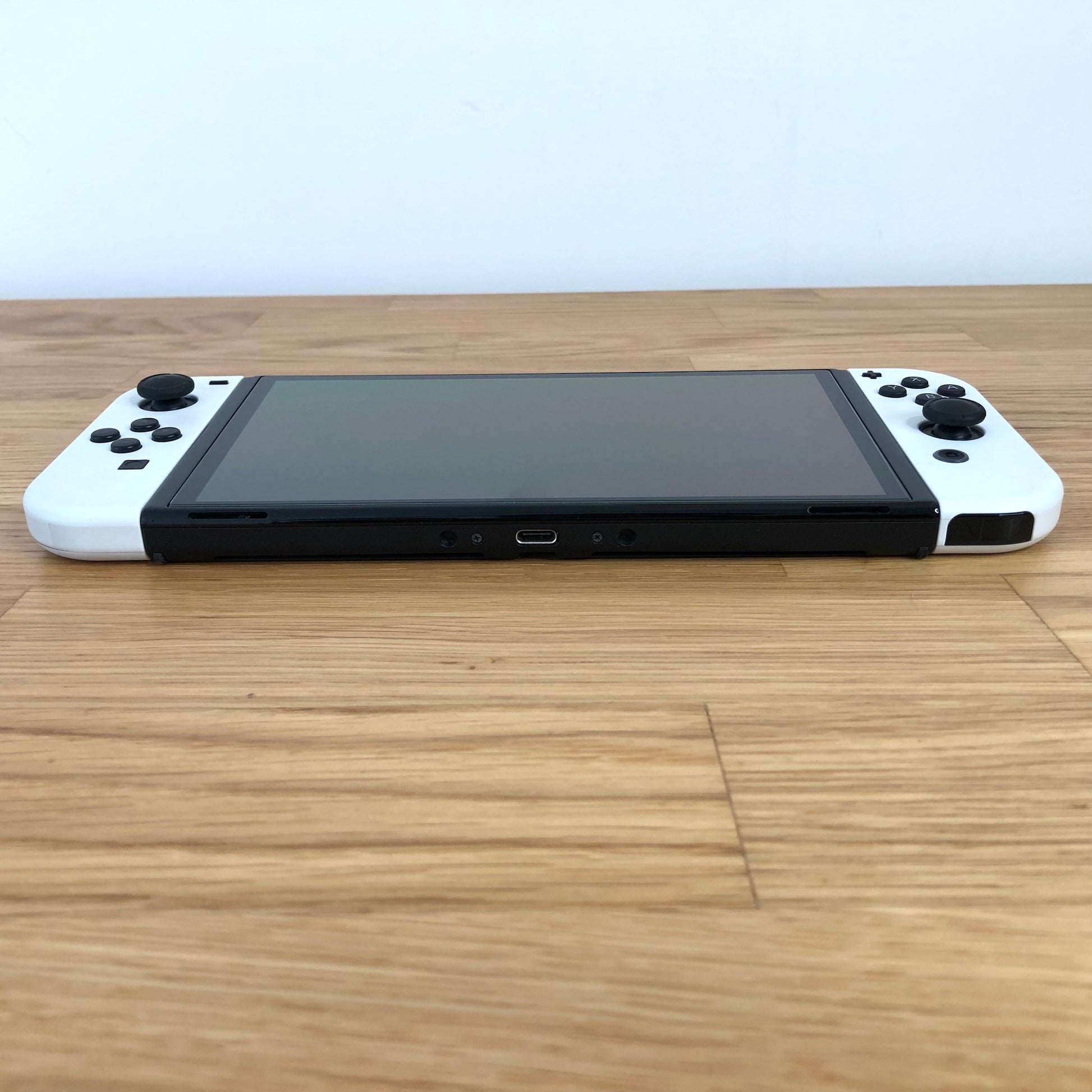 Bottom edge of Nintendo Switch OLED console showing USB-C charging port and Joy-Cons attached.