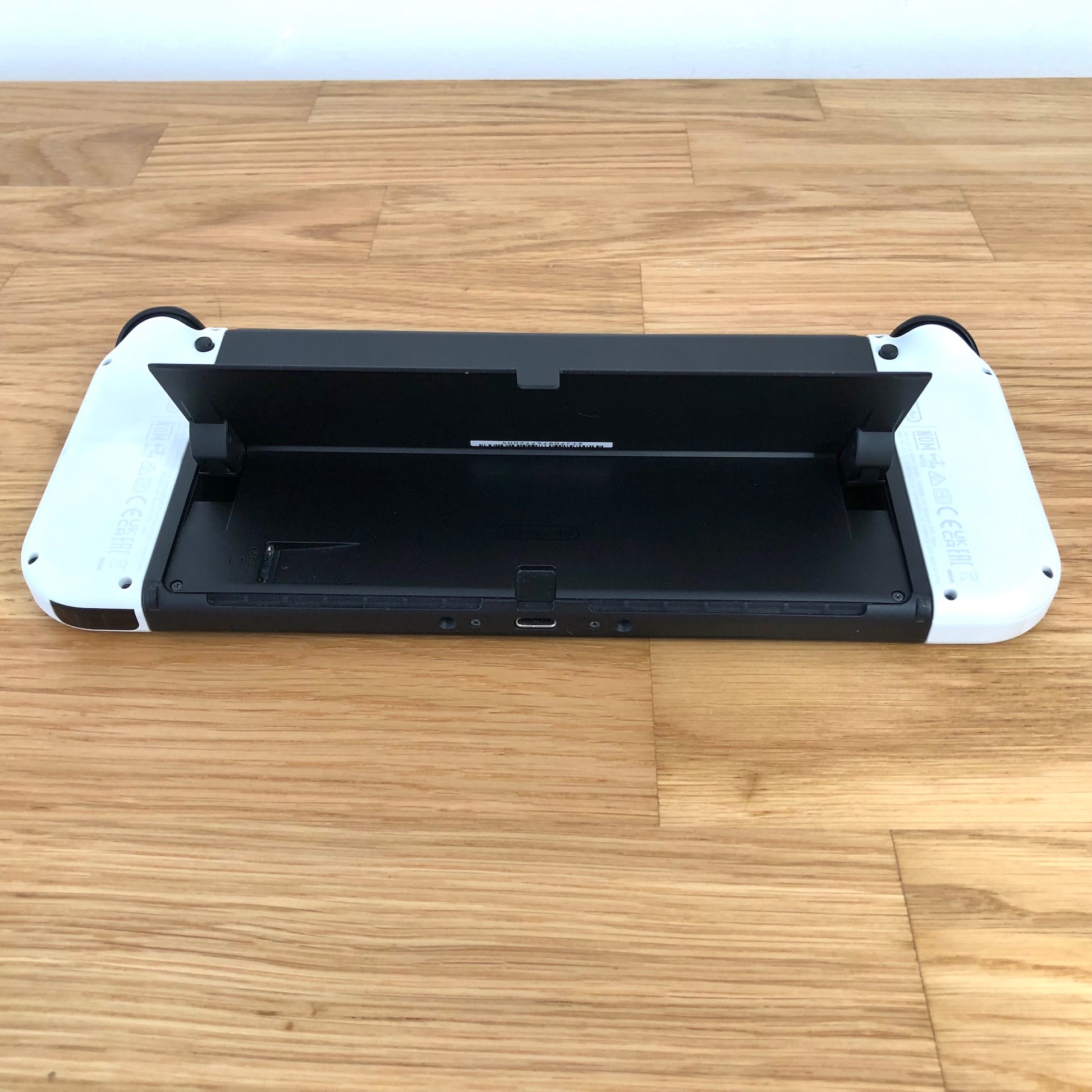 Bottom rear view of Nintendo Switch OLED with kickstand lifted, showing microSD slot, USB-C port and controls.