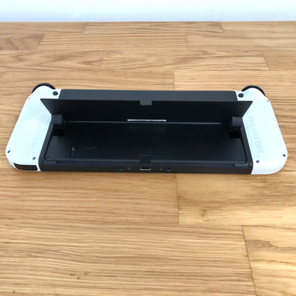 Bottom rear view of Nintendo Switch OLED with kickstand lifted, showing microSD slot, USB-C port and controls.