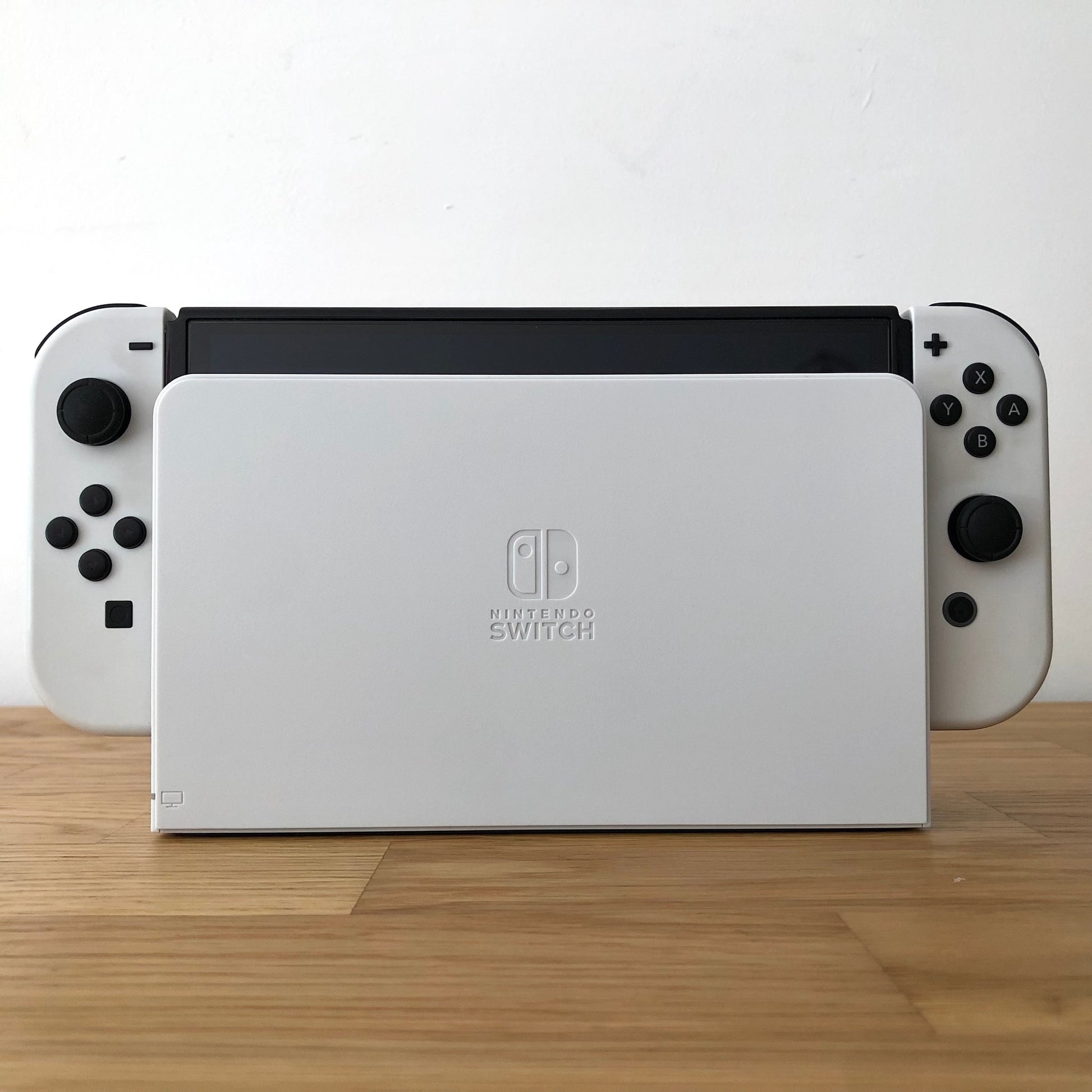 Front of Nintendo Switch OLED console docked, showing white Joy-Cons with button layout visible on both sides.