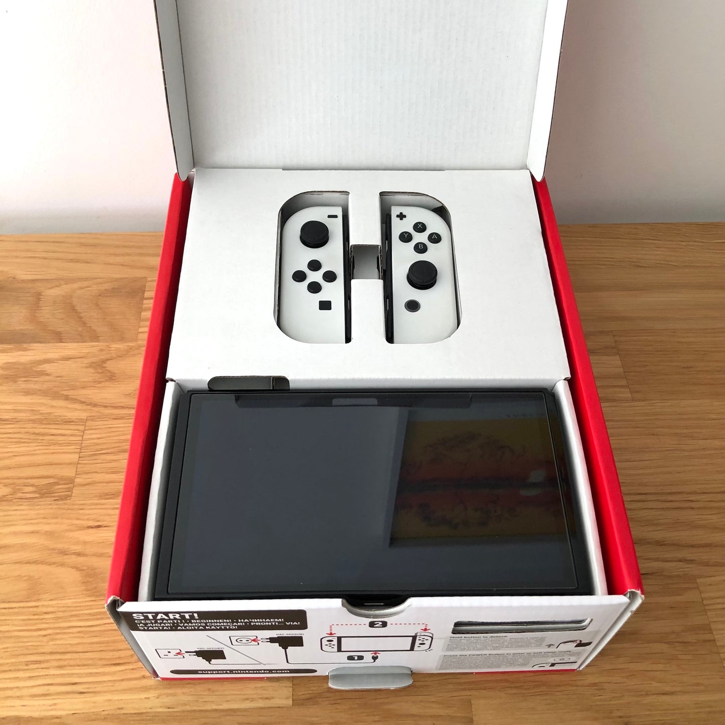Nintendo Switch OLED console in original box with lid open, showing screen and Joy-Cons neatly packed in top tray.