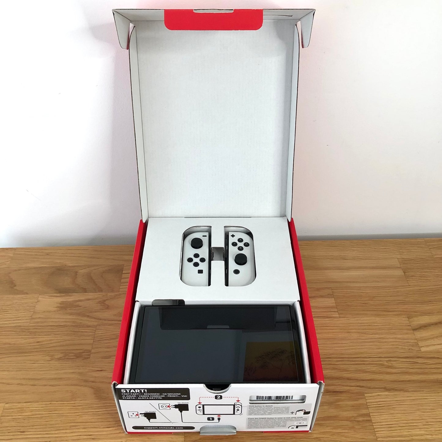 Nintendo Switch OLED console in original box with lid open, showing screen and Joy-Cons neatly packed in top tray.