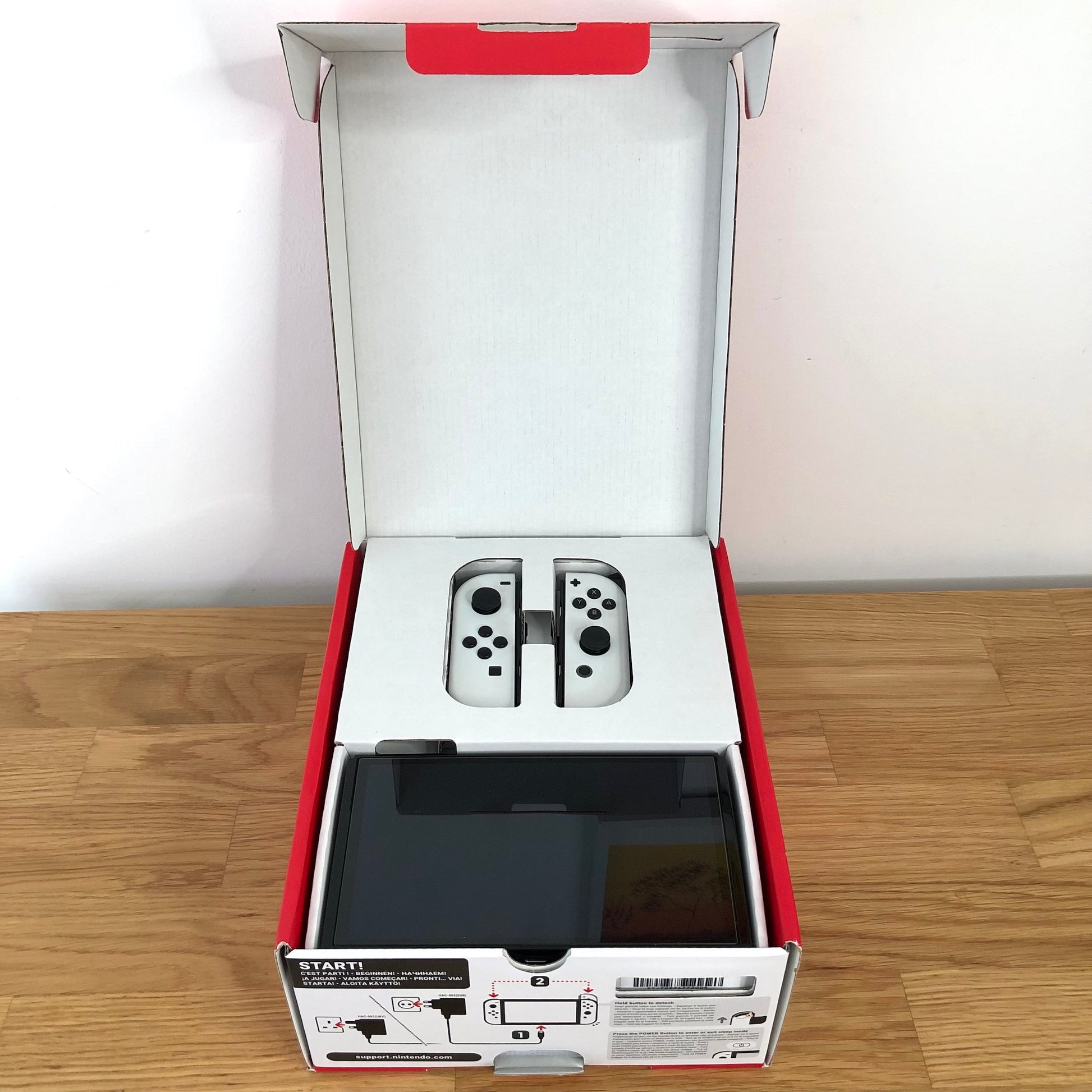 Nintendo Switch OLED console in original box with lid open, showing screen and Joy-Cons neatly packed in top tray.