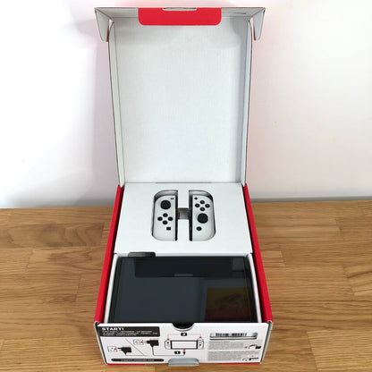 Nintendo Switch OLED console in original box with lid open, showing screen and Joy-Cons neatly packed in top tray.