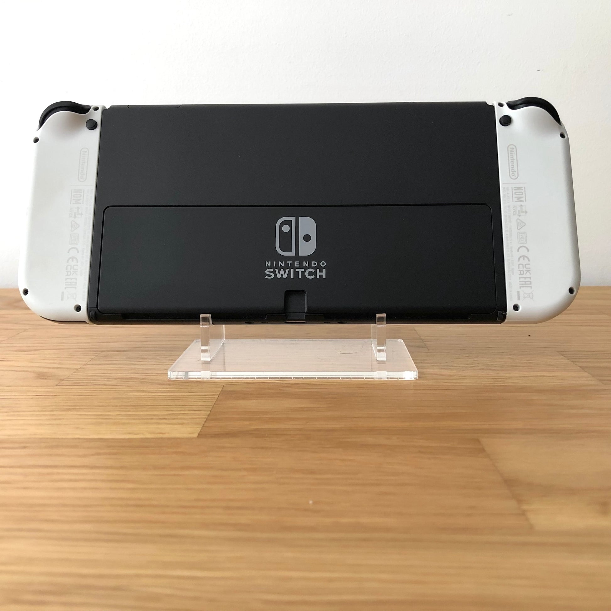 Back of Nintendo Switch OLED console with white Joy-Cons attached, showing logo and rear casing detail.