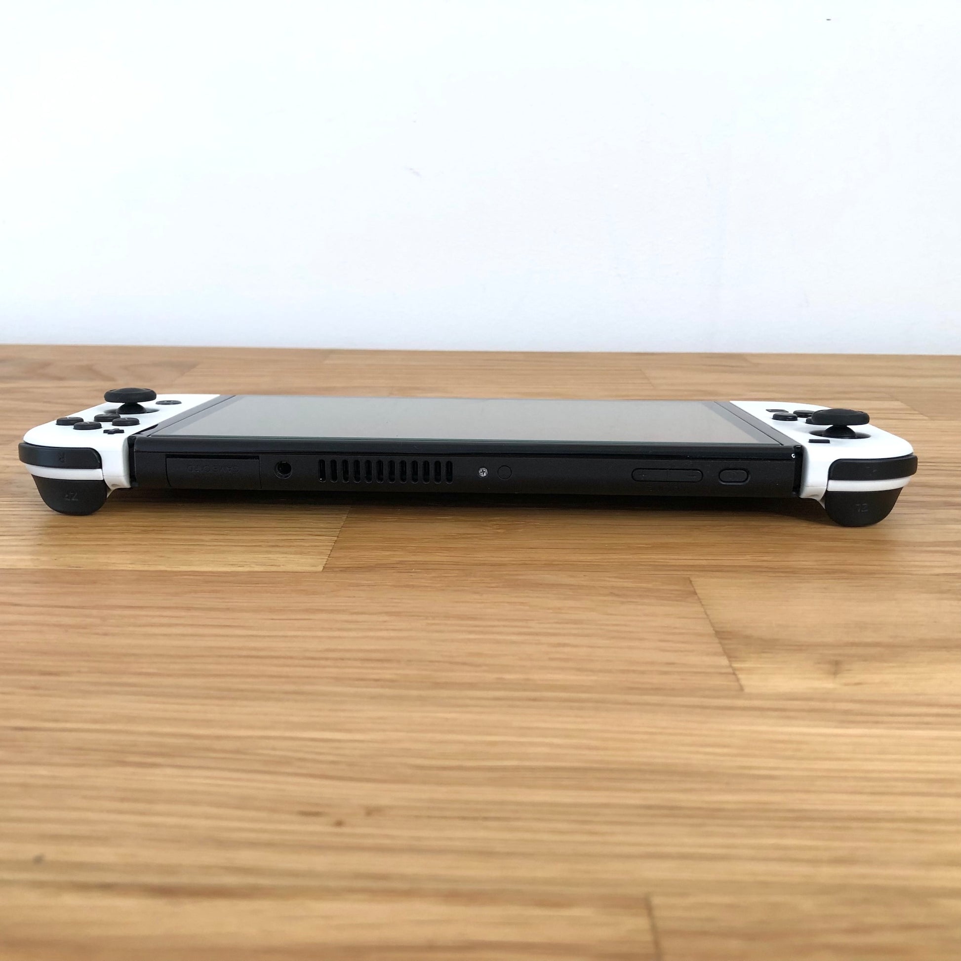 Back of Nintendo Switch OLED console with white Joy-Cons shown flat on table, logo and kickstand visible.