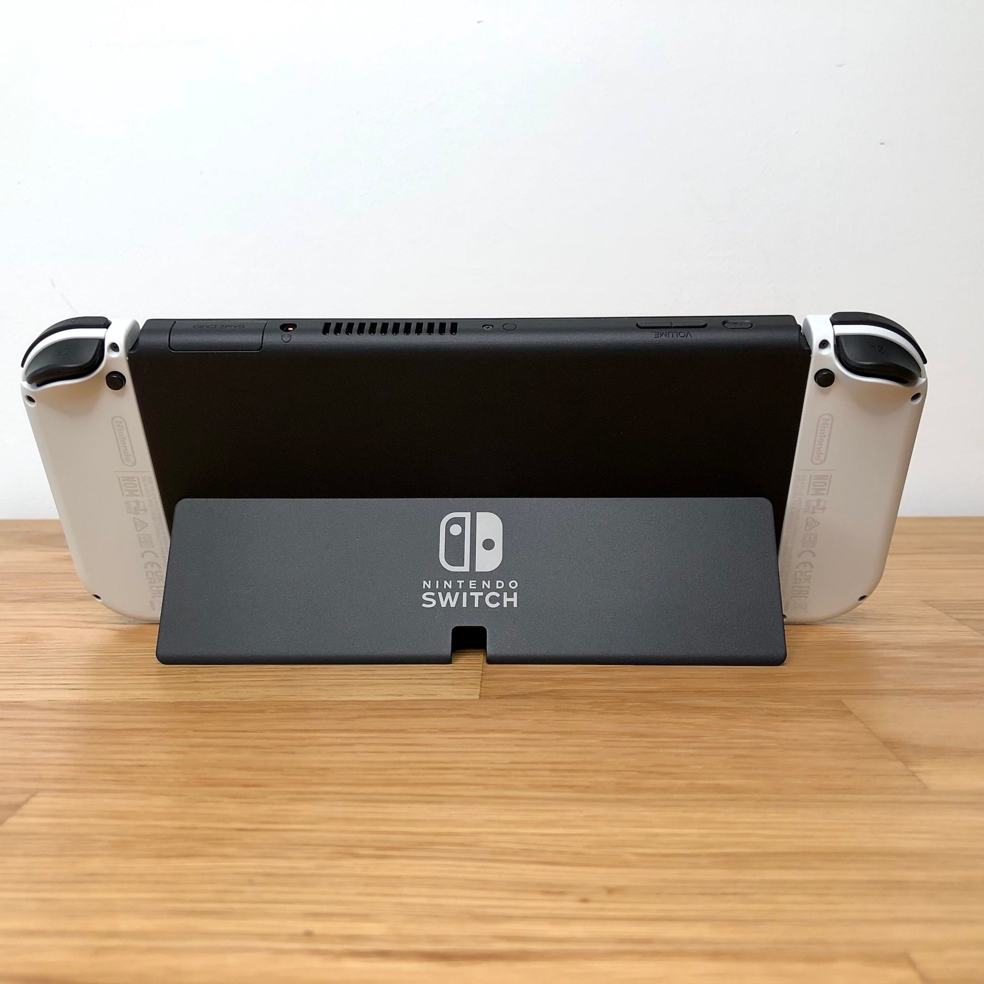 Back of Nintendo Switch OLED with kickstand open, showing logo, game card slot, vent and volume controls.