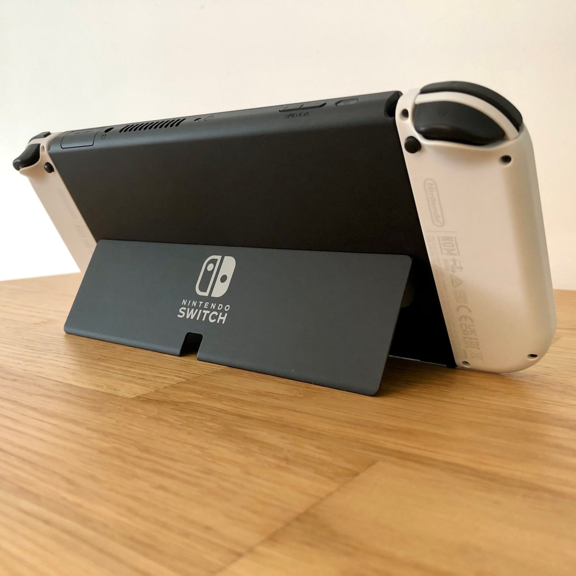 Angled rear view of Nintendo Switch OLED with kickstand open, showing logo, triggers and top-side buttons.