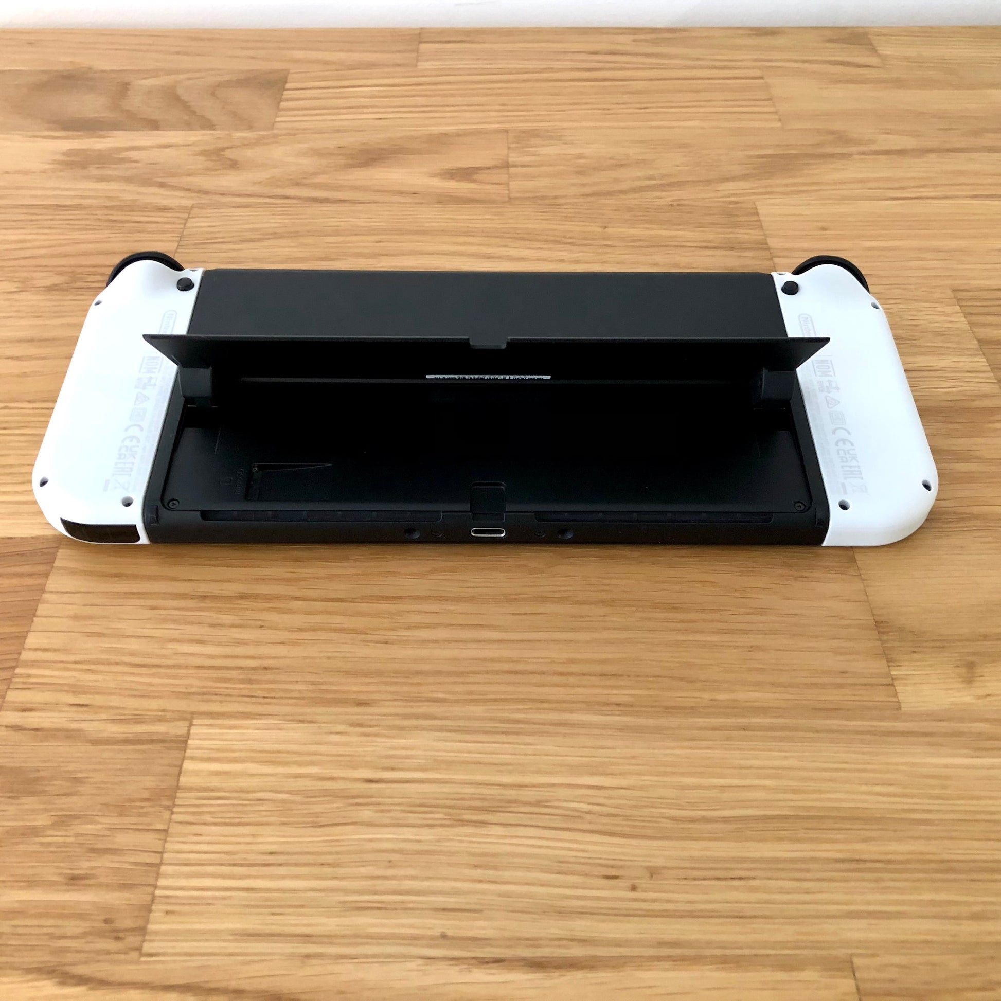 Bottom rear view of Nintendo Switch OLED with kickstand lifted, showing microSD slot, USB-C port and controls.