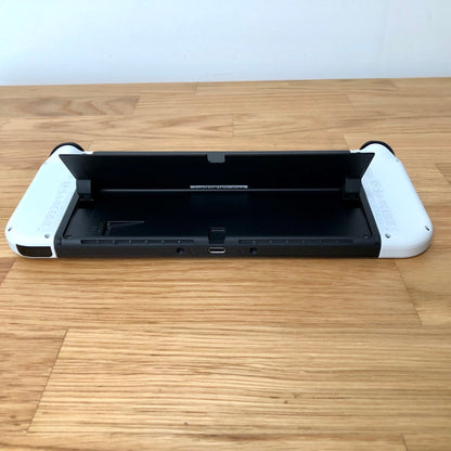 Bottom rear view of Nintendo Switch OLED with kickstand lifted, showing microSD slot, USB-C port and controls.