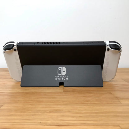 Back of Nintendo Switch OLED with kickstand open, showing logo, game card slot, vent and volume controls.