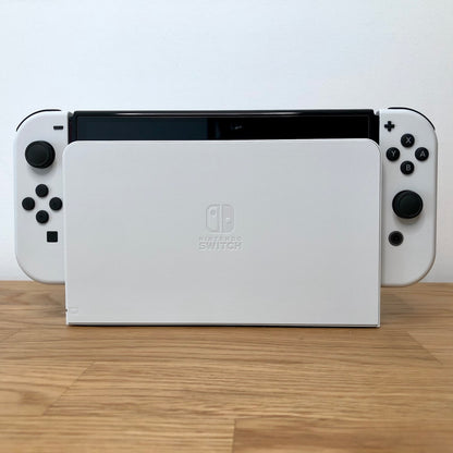 Front of Nintendo Switch OLED console docked, showing white Joy-Cons with button layout visible on both sides.