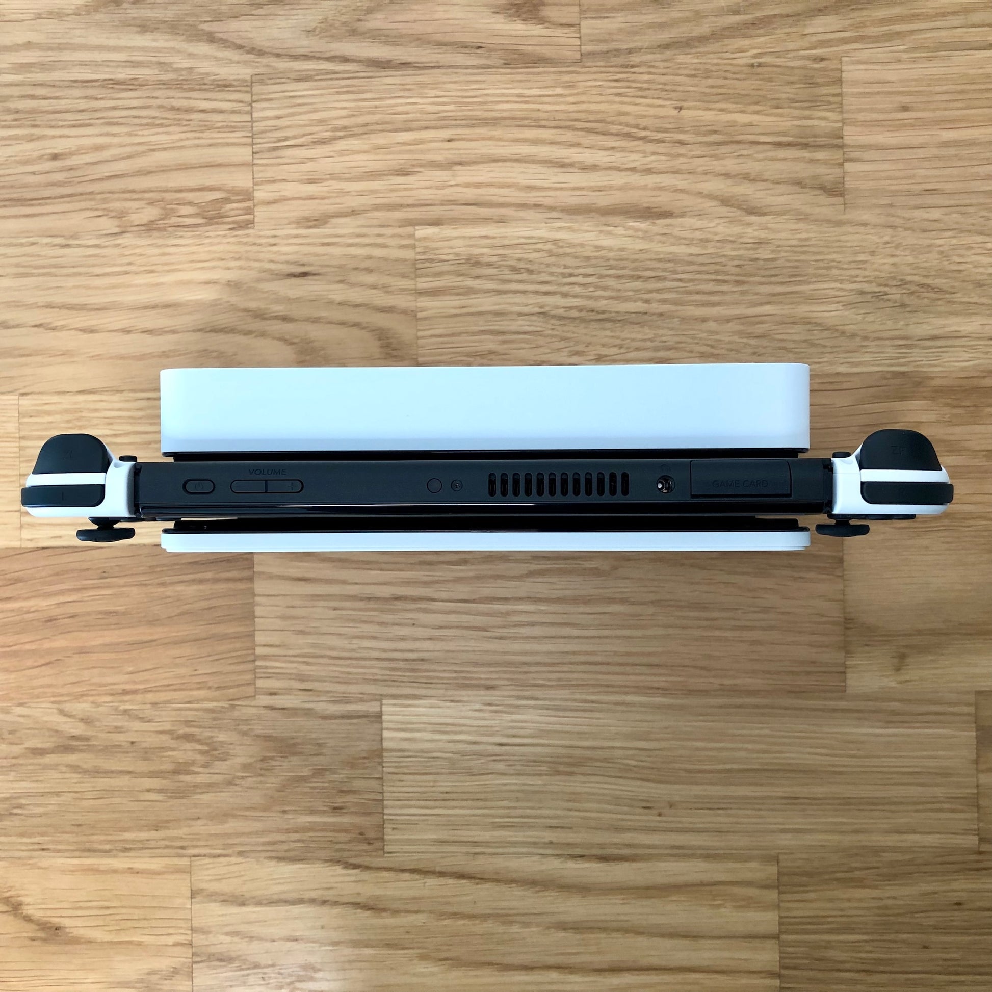 Top-down view of Nintendo Switch OLED in dock, showing Joy-Con triggers, game card slot and top-side buttons.