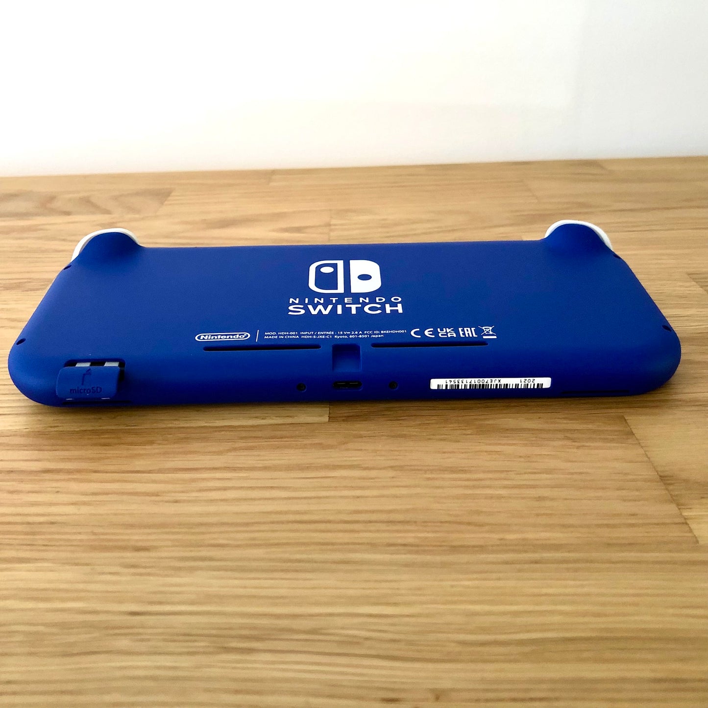 Angled bottom view of blue Nintendo Switch Lite console showing charging port, serial number and microSD slot.