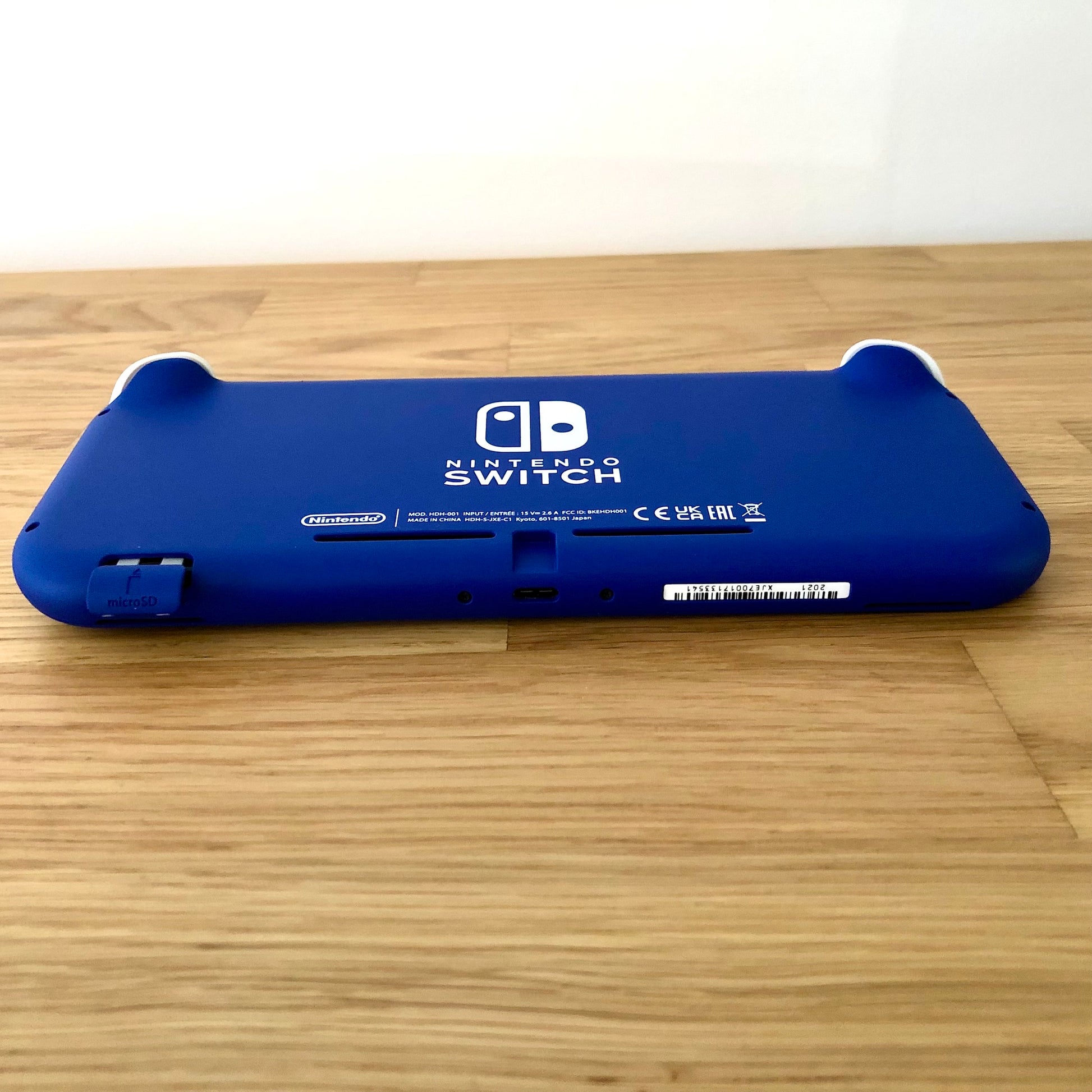Angled bottom view of blue Nintendo Switch Lite console showing charging port, serial number and microSD slot.