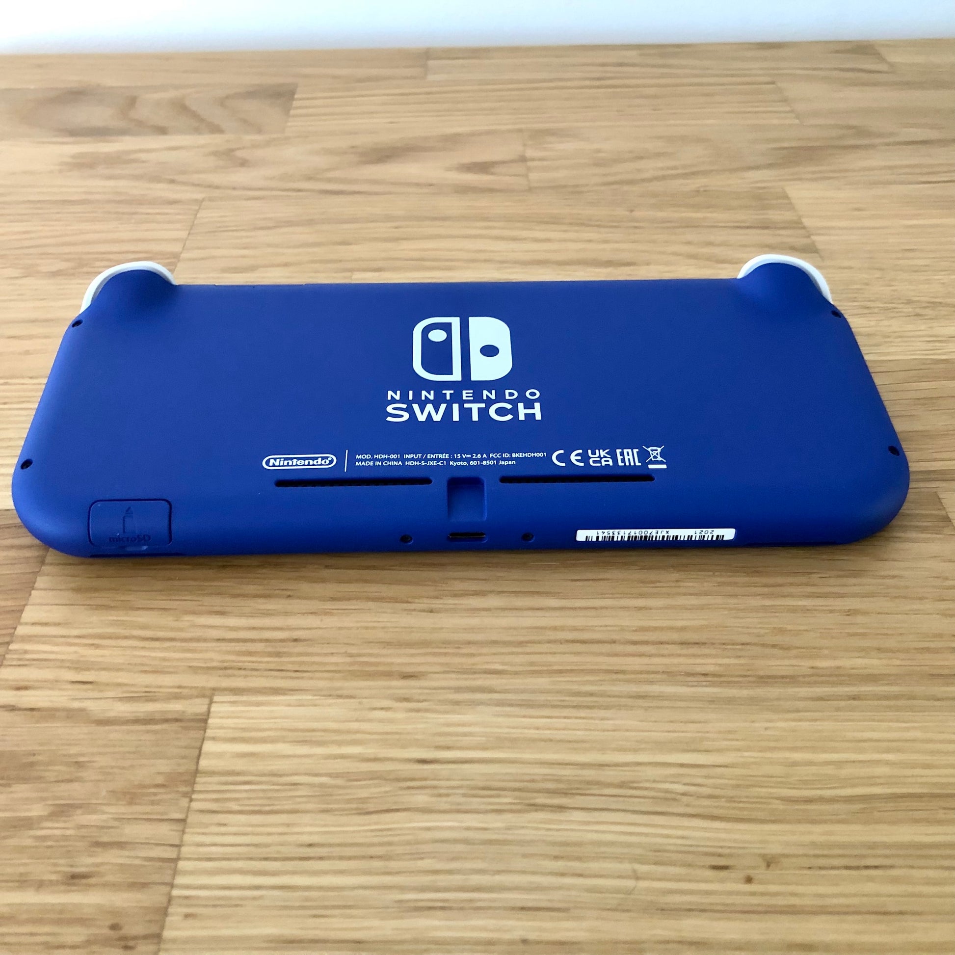 Back of Nintendo Switch Lite in blue, showing microSD slot, USB-C port, and product markings on a wooden surface.