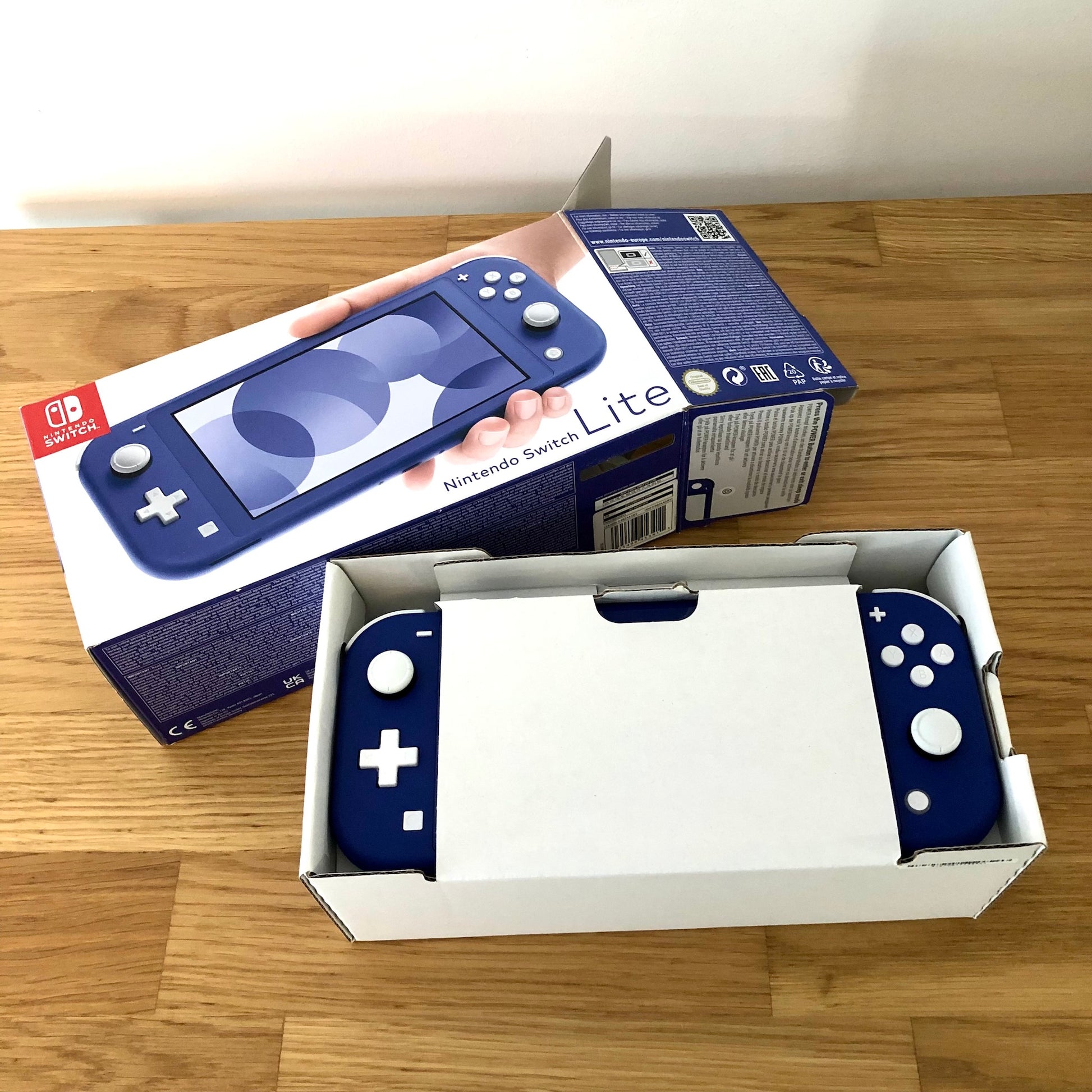 Nintendo Switch Lite in blue shown inside original packaging, with console partially visible in protective white insert.