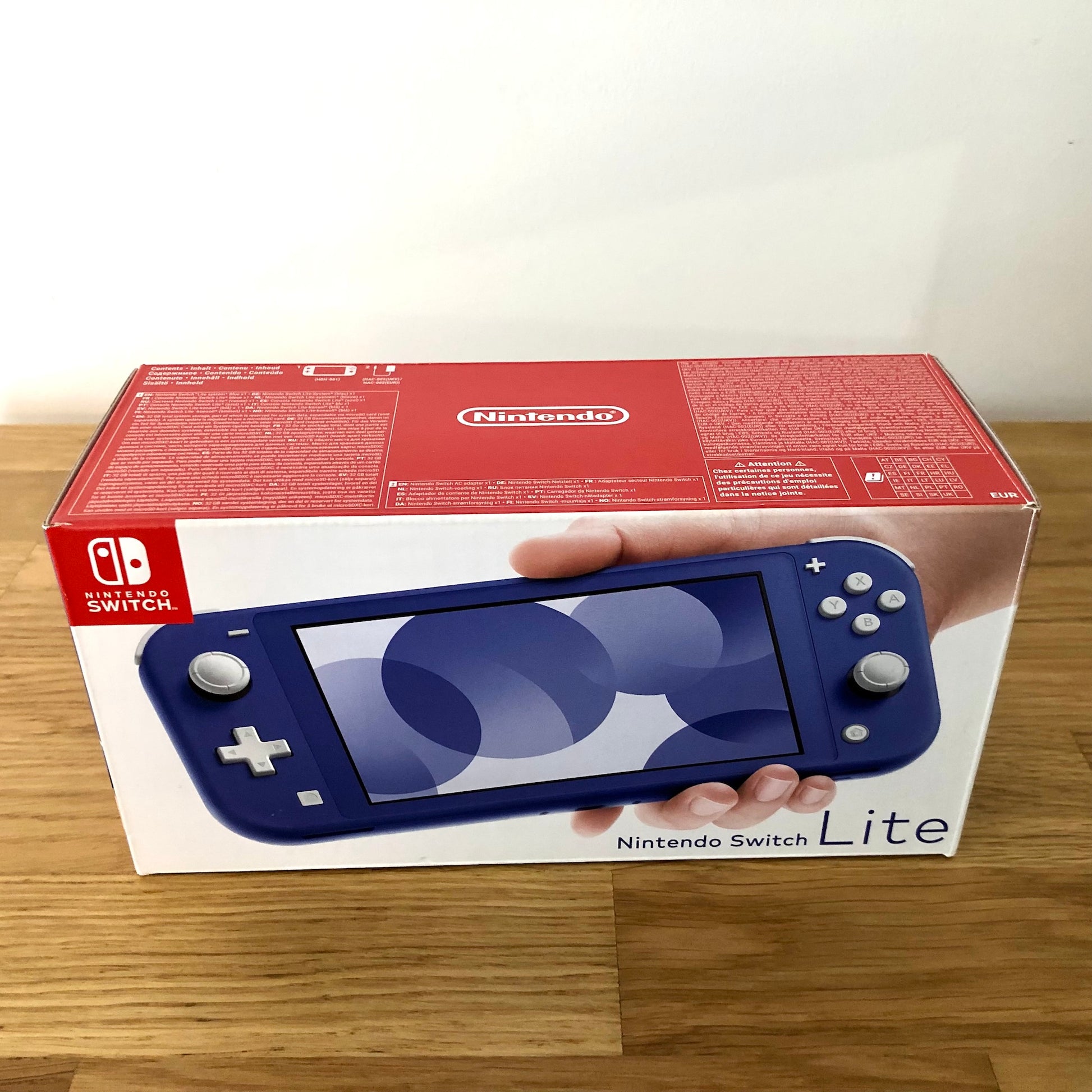 Front of Nintendo Switch Lite box in blue, showing product artwork and branding on a clean wooden surface.