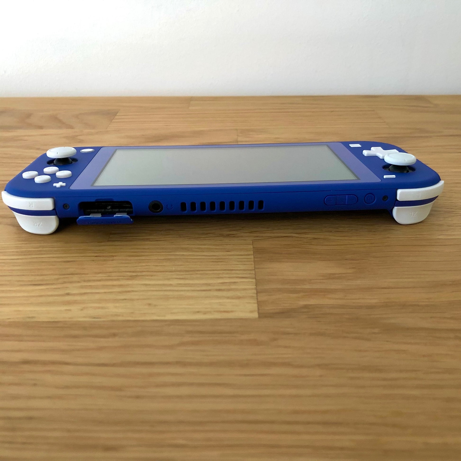 Top view of Nintendo Switch Lite in blue, showing game card slot, headphone jack, and volume/power buttons.