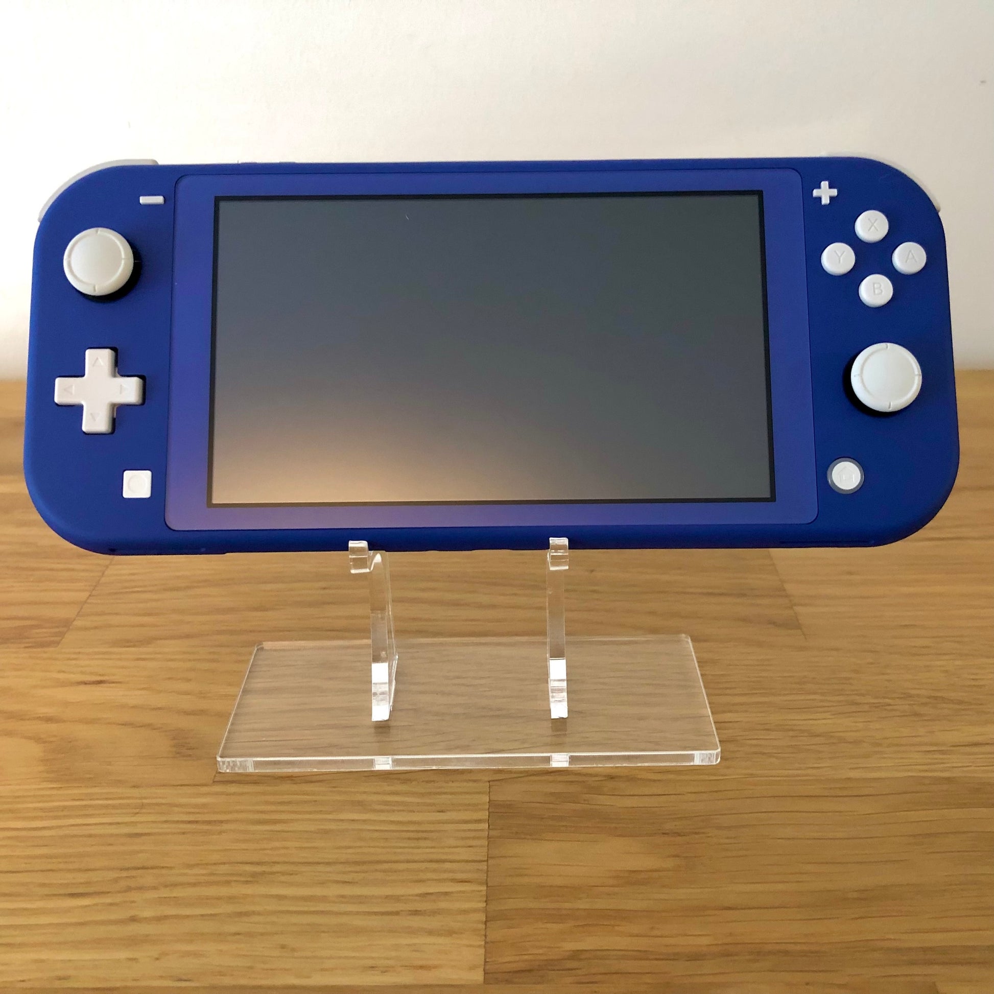 Front view of blue Nintendo Switch Lite console turned off, positioned upright on a clear display stand.