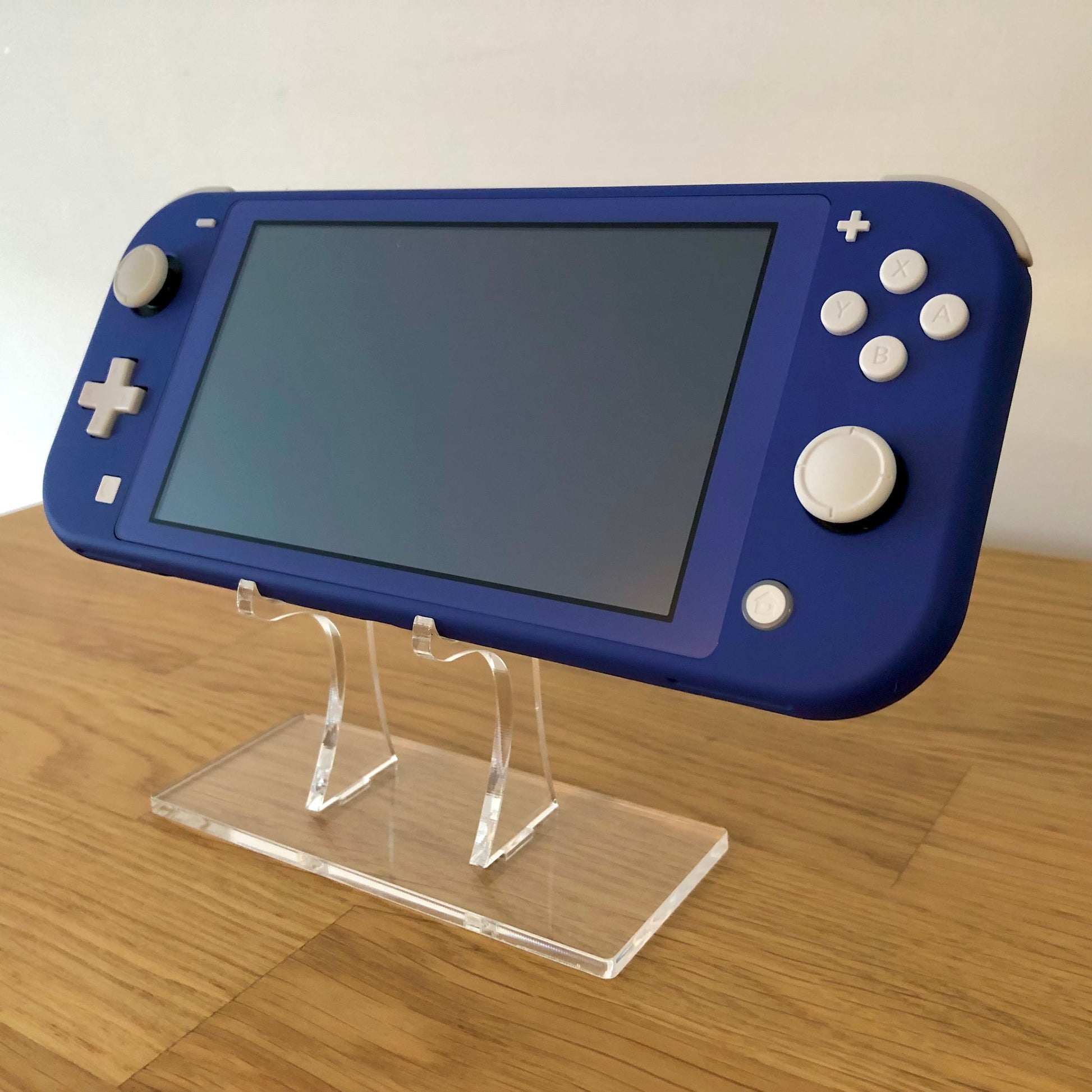 Angled front view of blue Nintendo Switch Lite showing buttons, thumbsticks and screen on clear stand.
