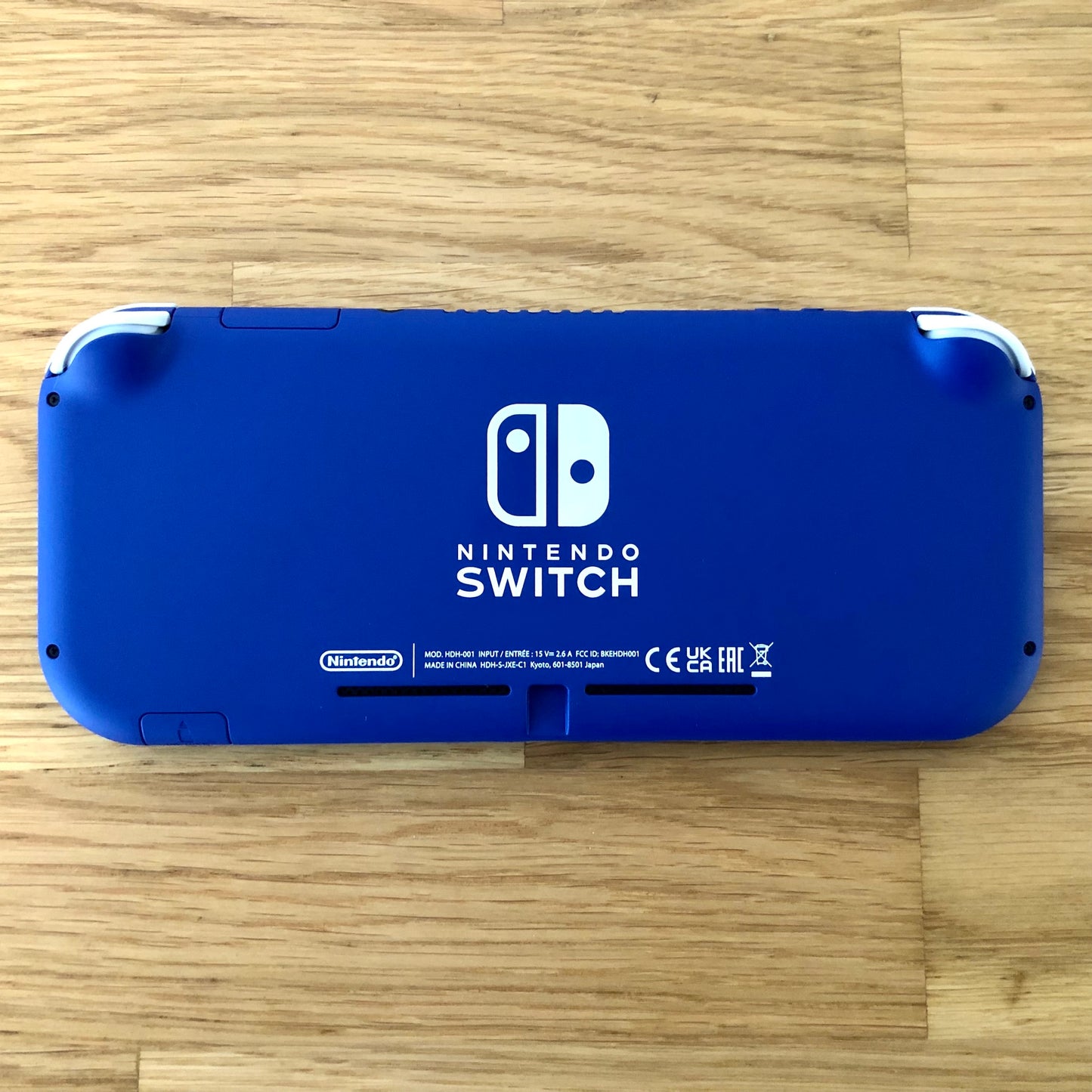 Back of blue Nintendo Switch Lite console placed flat, with logos, text and condition clearly shown.