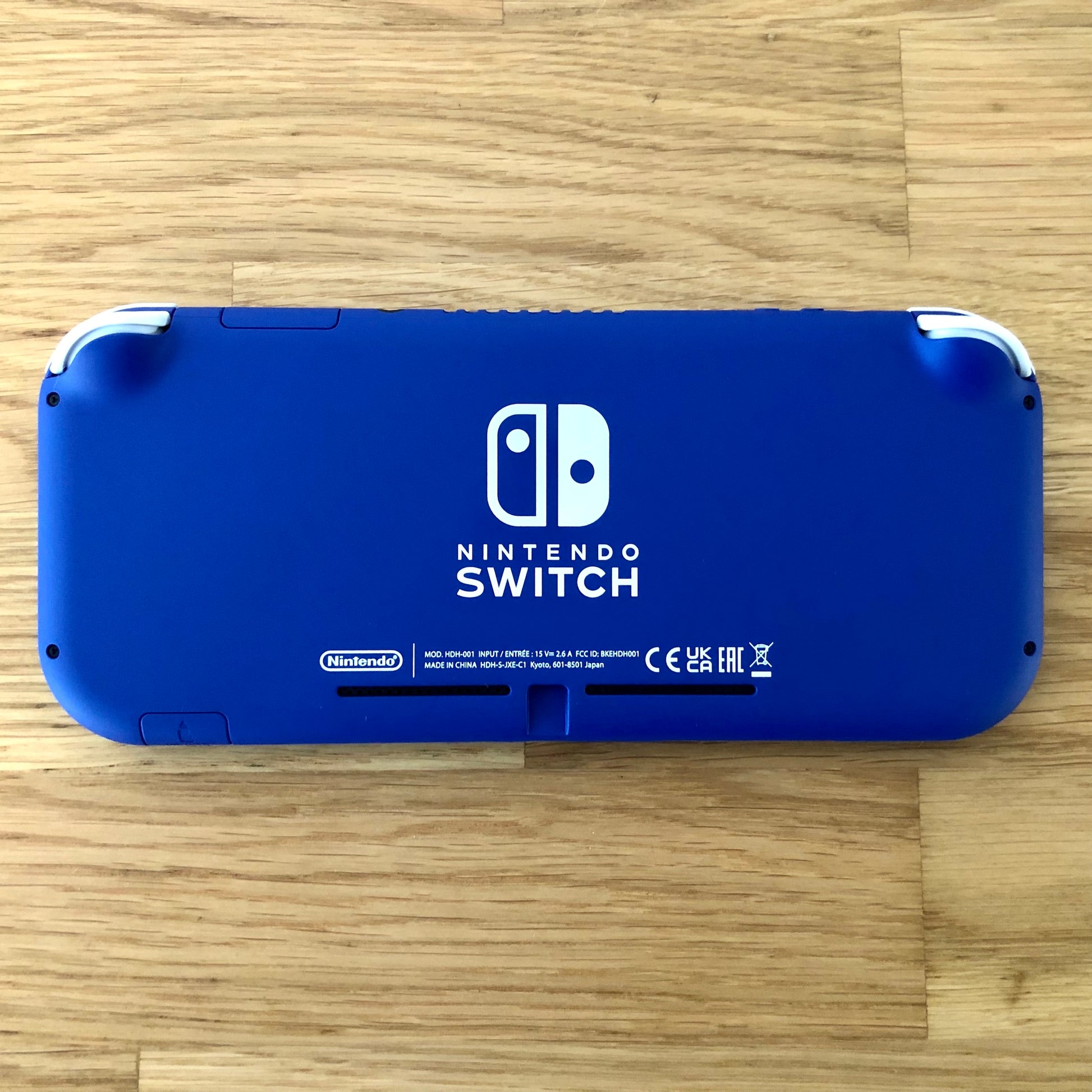 Back of blue Nintendo Switch Lite console placed flat, with logos, text and condition clearly shown.