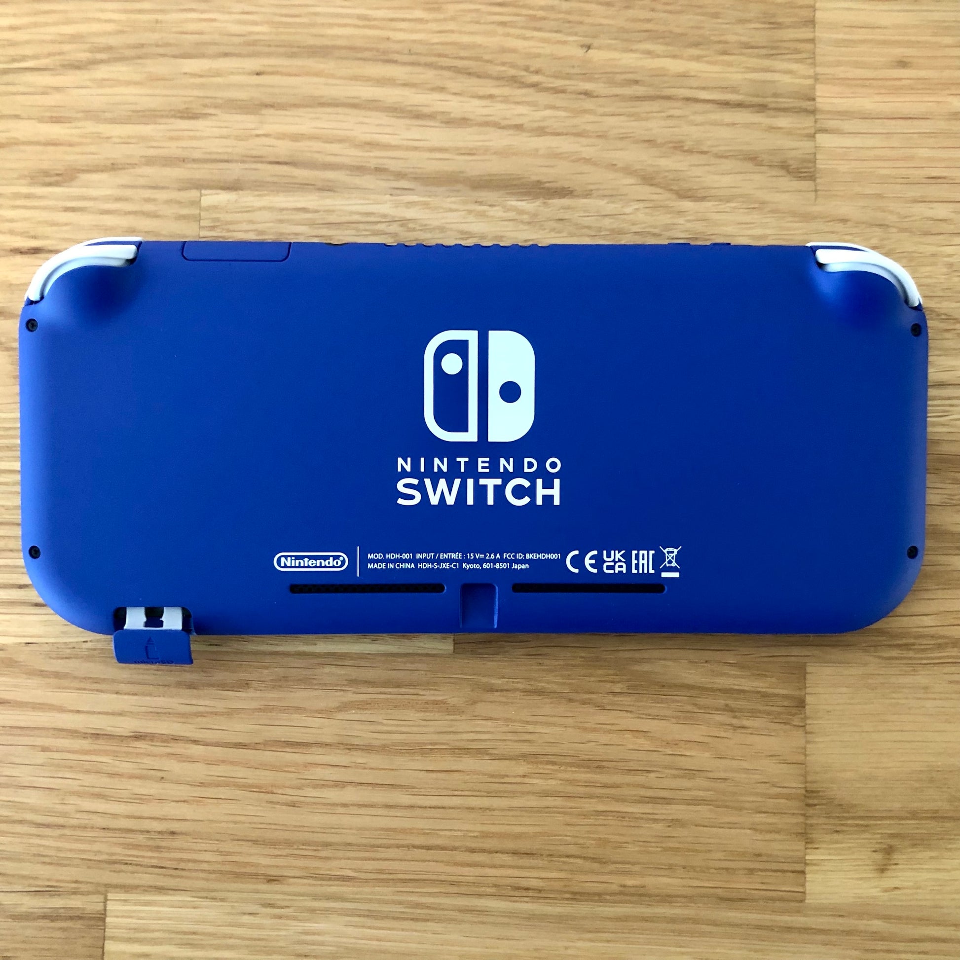 Blue Nintendo Switch Lite console laid flat with microSD slot cover open, showing full back design.